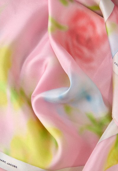 Tissu en soie rose avec imprimé floral pastel flou dans les tons jaune, vert, bleu et rouge, drapé avec douceur et montrant partiellement une étiquette Marc Jacobs.