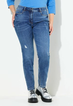 Jeans de corte ajustado, de lavado medio, con detalles desgastados y cinco bolsillos. Combinados con botas de plataforma plateadas y brillantes.
