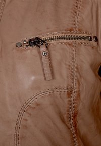 Béžová kožená bunda s kapsou na hrudi na zip, dekorativním šitím a měkkým úpletem. Kování zahrnuje stříbrný zip a knoflík.