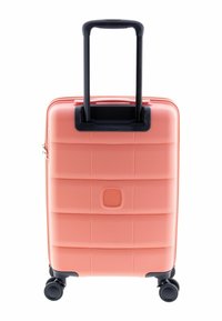 Valise rigide corail rose avec une surface texturée, une poignée noire rétractable et quatre roues noires pour faciliter la mobilité.