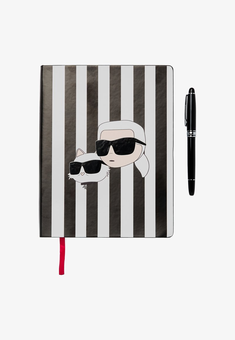 Notebook s čierno-bielymi pruhmi s karikatúrnymi postavičkami v slnečných okuliaroch. Obsahuje červenú stužku ako záložku a vedľa neho je čierne pero.