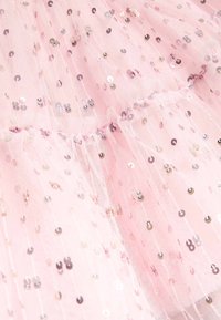 Rosa tule stof versierd met reflecterende pailletten in verschillende maten, wat een gelaagde textuur creëert met een zachte, luchtige uitstraling.