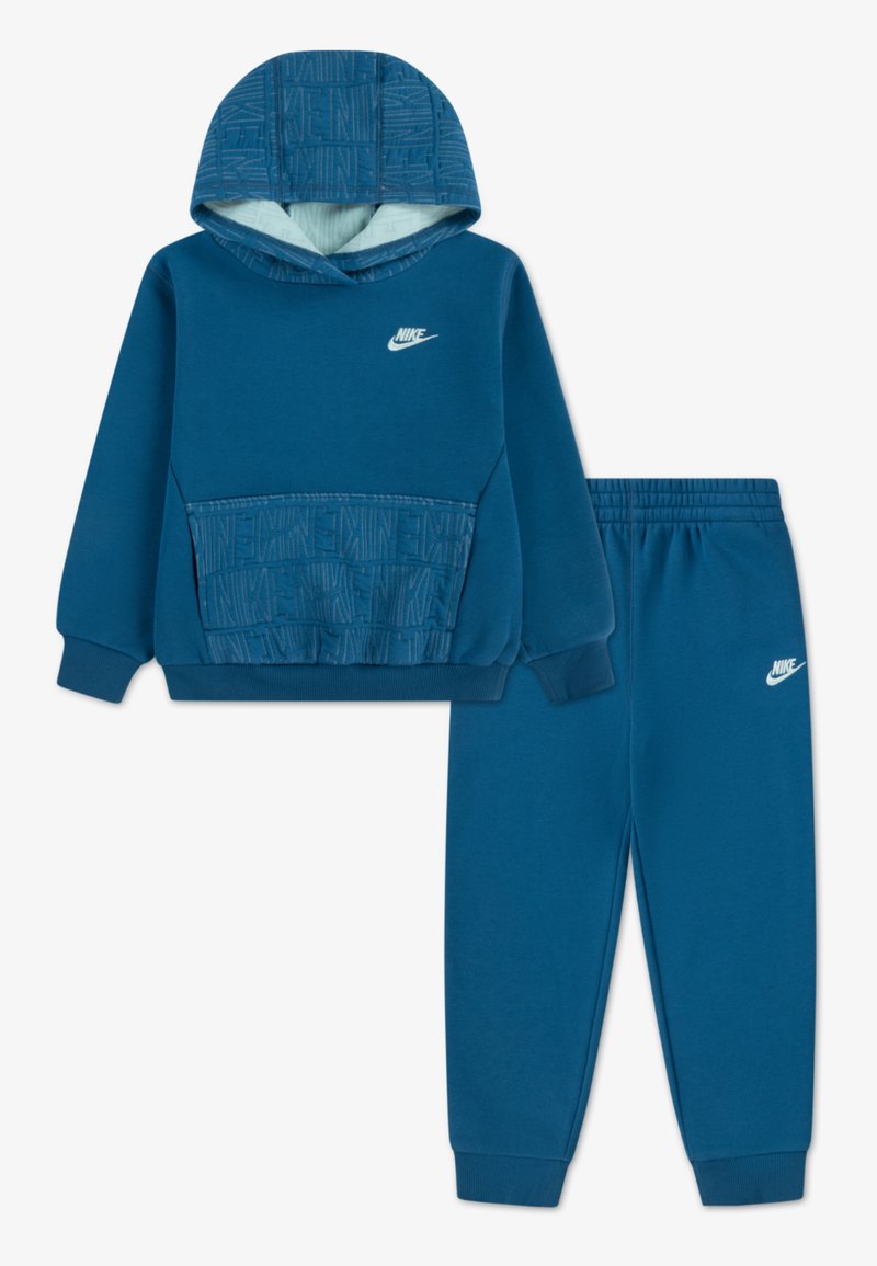 Modrý športový komplekt Nike s kapucňou, ktorý obsahuje textúrovanú prednú vrecko a logo, doplnený o zladené zúžené tepláky.