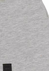 Tela de sudadera gris con una textura sutil y una pequeña etiqueta negra con "MSTRDS" en la esquina inferior.