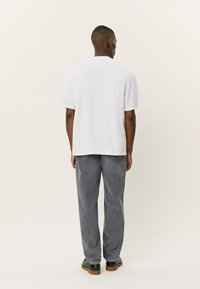 Tricou alb cu mânecă scurtă, fabricat din bumbac, asortat cu pantaloni gri cu croială lejeră. Design simplu și curat, fără modele sau grafice vizibile.