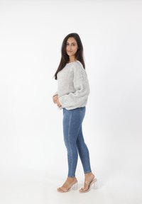 Lichtgrijze gebreide trui met brede mouwen, gecombineerd met aansluitende blauwe jeans. Heldere haksandalen maken de casual outfit compleet.