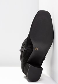 Stivaletto in suede nero con tacco quadrato basso, zip laterale, suola texturizzata e etichetta di dimensione "37" visibile sul tacco.