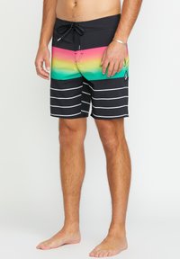 Shorts de bain noirs avec un motif dégradé de rose, vert et jaune, comportant des rayures blanches horizontales et une ceinture à cordon.