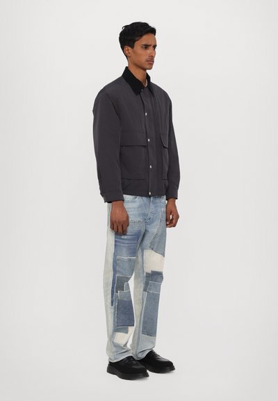 Szürke zakó gombos záródással és két elülső zsebbel, foltos farmernadrággal, különböző kék árnyalatokban. Fekete cipő teszi teljessé a megjelenést.