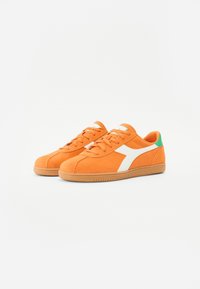 Oranje suede sneakers met witte accenten, voorzien van een groene hiel detail, rubberen zool en vetersluiting. Gladde textuur overal.