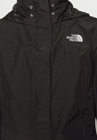 Zwarte waterdichte jas met capuchon en wit geborduurd The North Face-logo op de bovenkant van de linkerschouder.