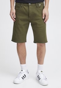 Olivengrüne Cargo-Shorts aus Baumwollmischung, im klassischen Schnitt, mit Gürtelschlaufen und seitlichen Taschen, kombiniert mit weißen Turnschuhen.