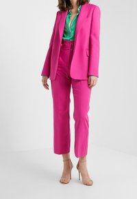 Fuchsia kostym med en stilig blazer och skräddarsydda byxor, kombinerat med en teal satinblus och beige klackar med remmar. Slätt tyg, modern passform.