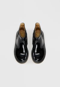 Bottines en cuir verni noir avec des panneaux latéraux élastiques, fermeture zippée et couture blanche contrastante sur la semelle. Fini lisse, bout rond.