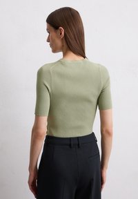 Ribbed, lyhythihainen toppi vaalean vihreänä, jossa on istuva siluetti ja pyöreä pääntie, yhdistettynä korkean vyötärön mustiin housuihin.
