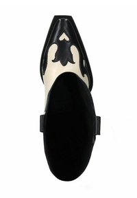 Chaussure à bout pointu avec un design noir et crème, présentant des motifs découpés complexes, une texture en cuir lisse, et une sangle élégante autour de la cheville.