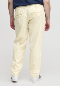 Lys gule bukser med avslappet passform, elastisk linning og to baklommer, kombinert med hvite sneakers med svarte striper.