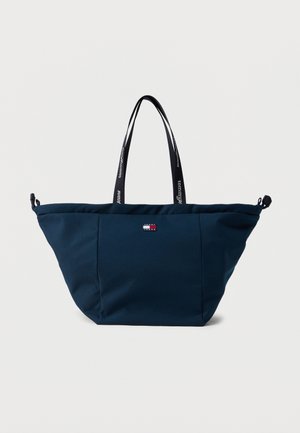 Grote donkerblauwe boodschappentas met zwarte handvatten, bedrukt met "tommy jeans" en een klein rechthoekig Tommy Jeans-logo in het midden aan de voorkant.