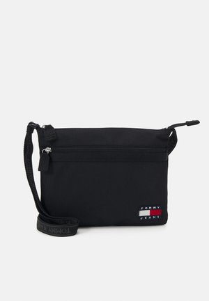 Czarna torebka na nadgarstek Tommy Jeans z zamkiem błyskawicznym, przednią kieszenią na zamek oraz ozdobnym paskiem i naszywką z logo.