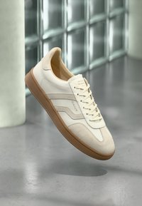 Weiße Sneaker mit Wildlederakzenten, Gummisohle und klassischem Schnürdesign. Mit dezentem Logo an der Seite.