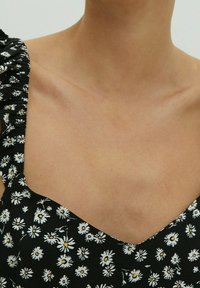 Vestido negro con flores blancas. Presenta hombros con volantes, escote en V y una textura ligera. Enfoque en los detalles del patrón floral.