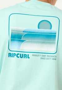 Camiseta verde menta con un gráfico de estilo retro que presenta olas azules y un sol. Incluye el texto "Ripcurl Quality Surf Products Since Sixty Nine".