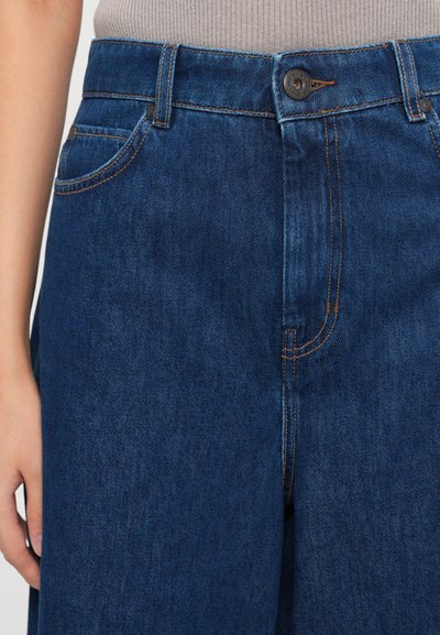 Denim jeans in dark blue with a smooth texture, featuring a button fly, side pockets, and contrast stitching.