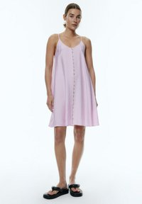 Helles rosa ärmelloses Kleid mit Knopfleiste, A-Linien-Form, strukturiertem Stoff und fließendem Design. Kombiniert mit schwarzen flachen Sandalen.