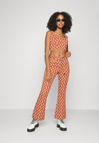 Conjunto de duas peças composto por um top cropped laranja e calças flare com um padrão em zigzag branco. A roupa apresenta uma textura suave e um design ajustado.