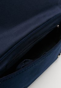 Interiér tašky z tmavě modré látky se zipem na kapsu a měkkou texturou. Okraj otvoru je lemován hladkým detailem.