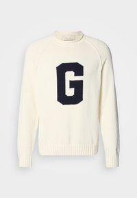 Cream sweater made of knit fabric featuring a navy blue 'G' logo design. It has a round neck and ribbed cuffs and hem.