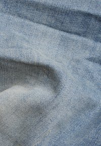 Ljusblå denimtyg med en subtil kornig textur, som har små veck och veckningar. Materialet verkar mjukt och flexibelt.