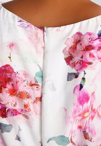 Floral dress featuring a white fabric with vibrant pink and red flower patterns, a rounded neckline, and a discreet back zipper closure.