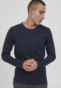 Tamno plava dugosleeve majica od mekanog pamuka, s okruglim izrezom i uskim rukavima. Minimalistički dizajn bez vidljivih uzoraka.