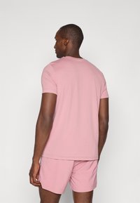 Lys rosa t-skjorte med korte ermer og rund hals, iført med matchende lys rosa shorts, synlig tekstur og rene linjer.