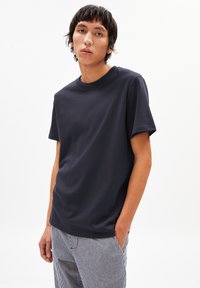 T-shirt à manches courtes bleu marine avec un col rond, fabriqué en coton doux, porté avec un pantalon rayé, offrant une coupe décontractée.