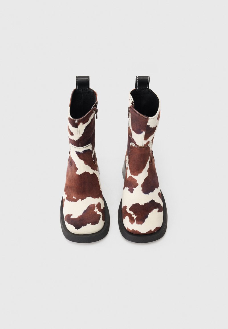 Cowhide ankle boots featuring a brown and white patchwork design, smooth texture, side zipper, and a black rubber sole.