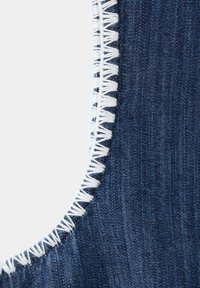 Gros plan d'un tissu en denim bleu foncé avec une couture zigzag blanche le long d'un bord courbé sur un fond clair.
