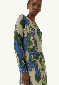 Langärmliges Kleid im mehrfarbigen Blumenmuster mit blauen, grünen und rosa Akzenten auf einem hellen Hintergrund. Es hat einen runden Halsausschnitt und eine figurbetonte Silhouette.