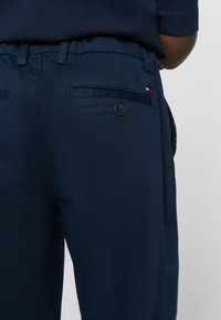 Marineblå bukser med en baglomme med knaplukning og en lille logoaccent. Stoffet har en glat tekstur og en skræddersyet pasform.