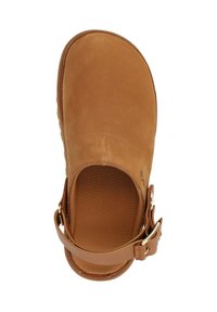 Zapato slip-on de ante color marrón claro, con una puntera amplia y redondeada, y una correa lateral que presenta un detalle de hebilla metálica. Textura suave y forro interior blando.