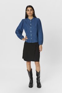 Chemise en jean à boutons avec des manches bouffantes, associée à une jupe portefeuille noire et des bottes noires jusqu'aux genoux. Design simple, couleurs classiques.