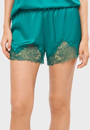 Shorts de satén color verde azulado con borde de encaje festoneado en el dobladillo, usados por una persona que muestra la parte superior de las piernas y las manos a los lados.