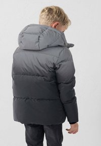 Chaqueta acolchada gris con capucha, que presenta un diseño degradado, textura acolchada y puños elásticos, llevada sobre vaqueros oscuros casuales.