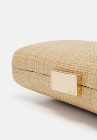 Pochette rectangulaire beige tissée avec des bords arrondis et un fermoir rectangulaire doré gravé de petites lettres "PRF" sur fond blanc.