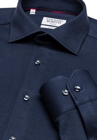 Marineblauwe slim-fit shirt gemaakt van kreukvrije stof, met een klassieke kraag, strakke knopen en omrolbare mouwdetails.