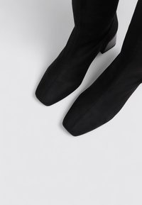 Black suede ankle boots with a square toe and a block heel, featuring a smooth texture and minimal stitching detail along the side.