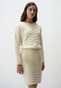 Gebreide trui met een brede ronde hals en lange mouwen, gecombineerd met een bijpassende rok; kleur crème met textuurpatronen in zigzag en stippen.
