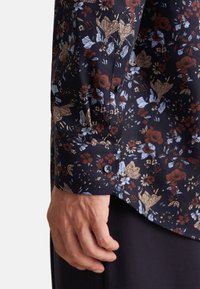 Marineblomstret skjorte med brune, blå og gyldne mønstre, der har en knapmanchet og blødt stof, designet med en asymmetrisk kant.