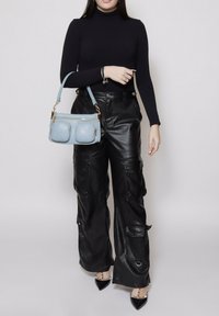 Pantaloni cargo in finta pelle nera con multiple tasche, abbinati a un dolcevita nero aderente e una borsa a tracolla azzurro chiaro con due tasche con zip.